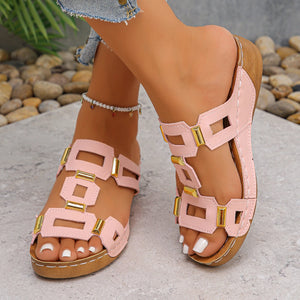 Pink and brown sandals worn by a person with a stone and plant background