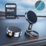 Foldable black car phone holder on a car dashboard with a blurred outdoor background.