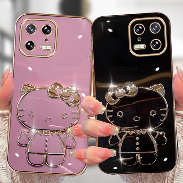 Two mobile phone cases with Hello Kitty designs, one in pink and one in black, each featuring a mirrored base with a ring holder.