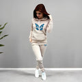 Woman wearing a beige tracksuit with blue butterfly designs on a gray background