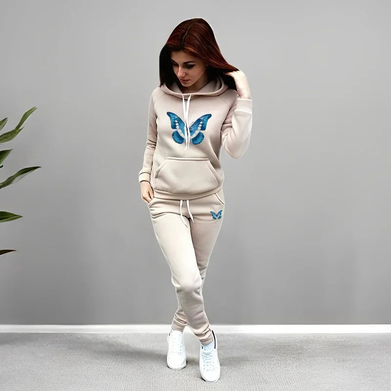 Woman wearing a beige tracksuit with blue butterfly designs on a gray background