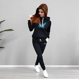 Woman wearing a black hoodie and pants with a blue logo, standing against a gray background.